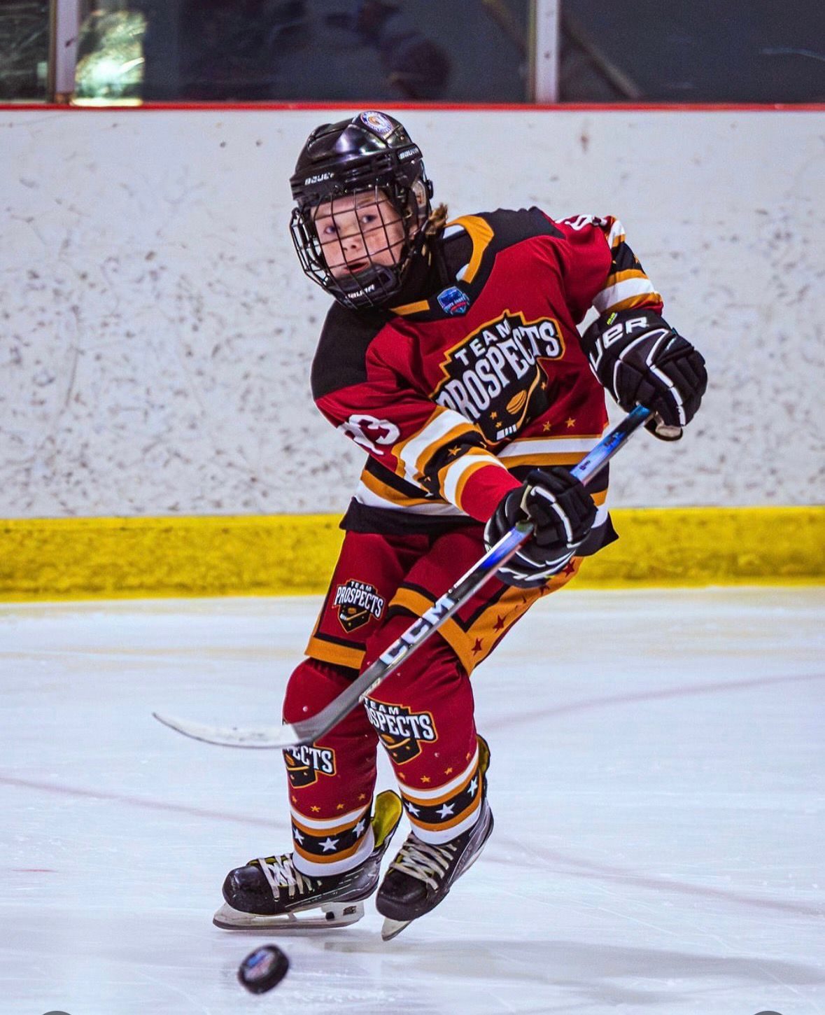 A Team Prospects player in a maroon and gold jersey winds up to shoot the puck during a game